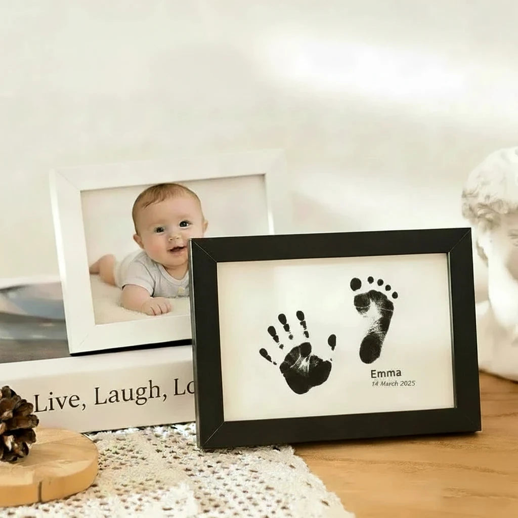 Two light wood frames on a tabletop, one showing a baby photo and the other displaying black baby footprint prints on a white insert with the name Emma. Text at the top reads 'Baby Footprint Photo' and 'Frame Record Beautiful Moments in Life.